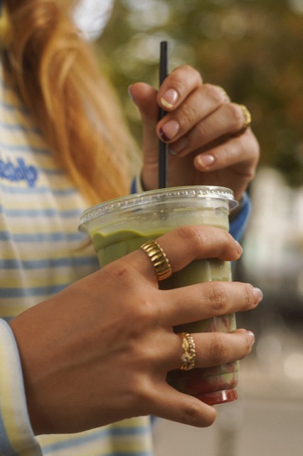 Hände mit Ringen halten einen Matcha-Eisbecher